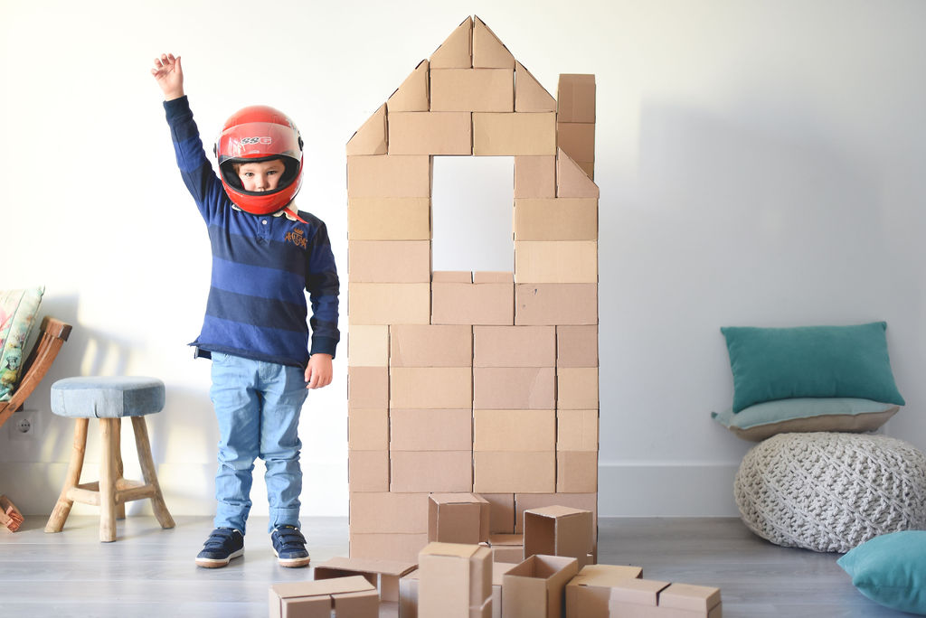 Criança com capacete ao lado de casa de blocos de cartão