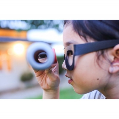 Criança com óculos a olhar através de um tubo branco ao ar livre