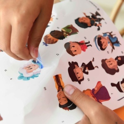 Mãos a colar autocolantes coloridos de personagens animadas numa folha branca