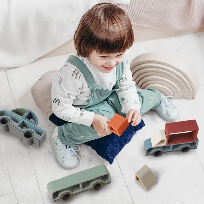 Criança a brincar com camiões de brinquedo de plástico colorido no chão de madeira clara