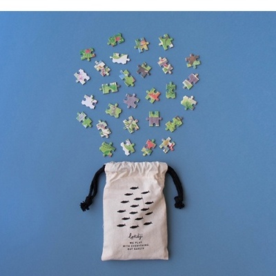 Peças de puzzle colorido e saco de pano branco com cordões pretos num fundo azul