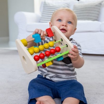 Bebé a brincar com ábaco de madeira colorido sentado no chão cinzento em sala de estar