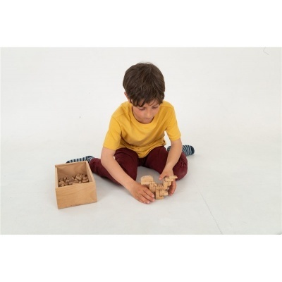 Menino a brincar com blocos de madeira sentado no chão branco com caixa de blocos ao lado.