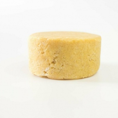 Queijo redondo amarelo claro com textura granulada sobre fundo branco