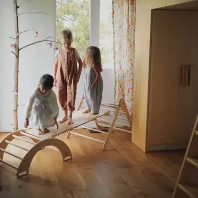 Crianças a brincar numa estrutura de madeira para escalar e apanhar balanço num quarto com decoração simples.