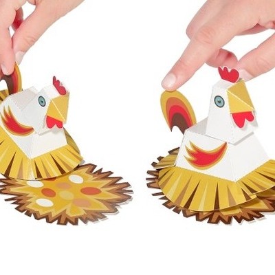 Dois brinquedos em forma de galinha em papel colorido, manipulados por mãos.
