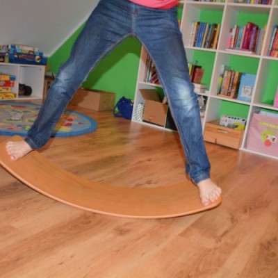 Balanço de madeira curvado usado por criança em divisão verde com prateleiras e chão de madeira