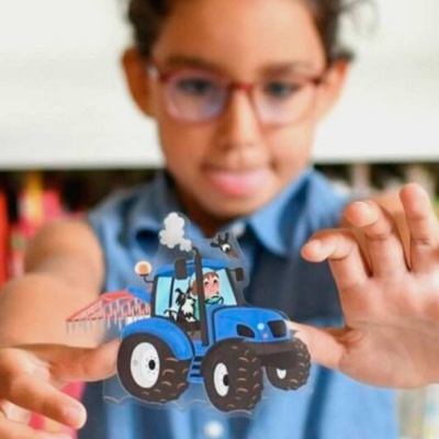 Menina segura brinquedo de papel de trator azul com vaca