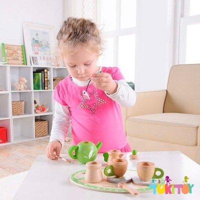 Menina a brincar com conjunto de chá de madeira numa mesa branca em sala com sofá e estante