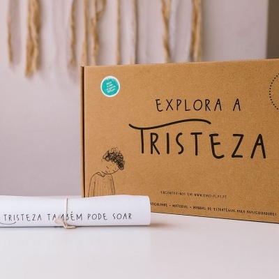Caixa de papelão com texto 'Explora a Tristeza' e rolo de papel com texto 'A Tristeza Também Pode Soar'