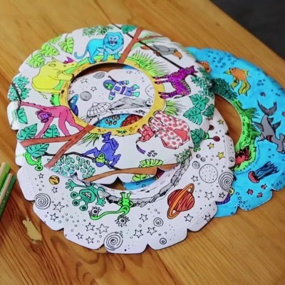 Rosetas de papel para colorir com padrões de animais e planetas sobre mesa de madeira com canetas coloridas