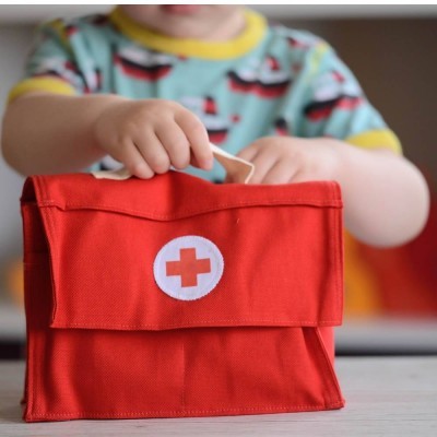 Estojo de primeiros socorros vermelho com cruz vermelha em branco, segurado por criança