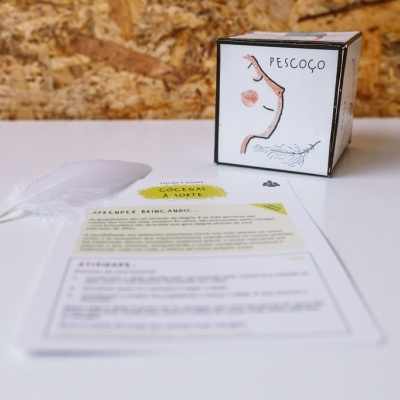 Produto em caixa branca com ilustração e texto PESCOÇO, folha com texto e colher plástica sobre superfície branca