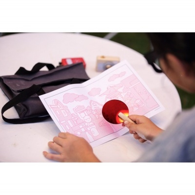 Pessoa segurando raquete de pingue-pongue pequena sobre papel com desenhos cor-de-rosa numa mesa branca ao ar livre