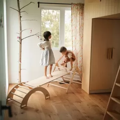 Brinquedo de madeira com crianças a brincar num quarto com chão de madeira e janela com cortina colorida