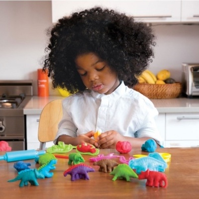 Criança a brincar com massinha e dinossauros coloridos numa cozinha