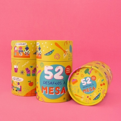 Três latas amarelas com desenhos coloridos e texto '52 DESAFIOS À MESA THE HAPPY GAME'