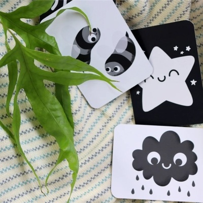 Três cartões com desenhos a preto e branco sobre uma manta às riscas bege e azul, com uma folha verde