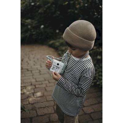 Criança com camisola às riscas e gorro a ver fotografia numa câmara instantânea junto a vegetação.