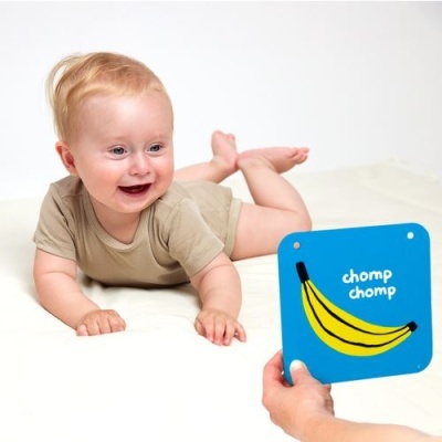 Bebé de body bege a olhar para placa azul com banana e texto 'chomp chomp'