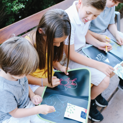 Crianças desenhando em tapetes reutilizáveis coloridos sentadas num banco exterior