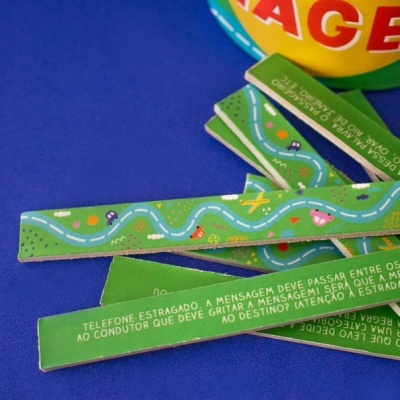 Tiras verdes com estrada e carros, texto em português, sobre fundo azul com parte de objeto redondo colorido