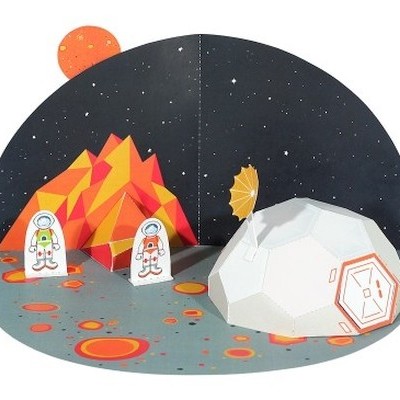 Cenário espacial de papel com astronautas, vulcão geométrico e módulo lunar branco.