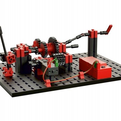 Modelo mecânico com peças plásticas vermelhas e pretas numa base preta perfurada