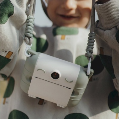 Câmara fotográfica compacta pendurada no pescoço de uma criança com roupa branca com padrão verde