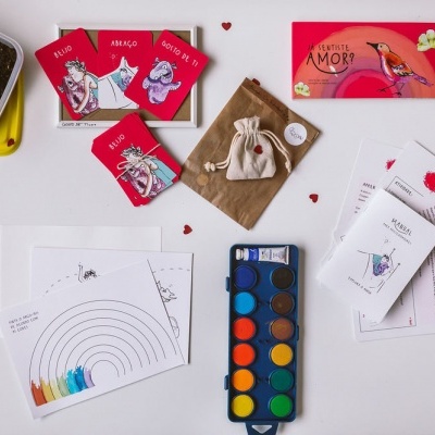 Conjunto de cartões, paleta de tinta aquarela, folhas com desenhos e saco de tecido numa superfície branca