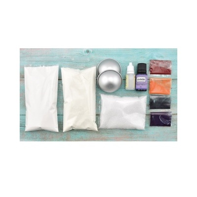 Kit de materiais para produção de cosméticos ou sabonetes, incluindo pós coloridos, embalagens metálicas e frascos com líquidos sobre madeira azul.