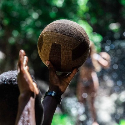 Bola de voleibol castanha sendo segurada por mãos num ambiente ao ar livre com vegetação