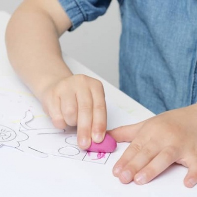 Criança a apagar desenho num papel com borracha rosa na mesa branca