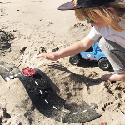 Criança a brincar com estrada de brinquedo e carros em areia na praia