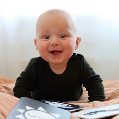 Bebé sorridente a brincar com cartões educativos em cama com manta castanha