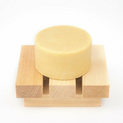 Sabonete redondo bege num suporte de madeira clara com três ripas em fundo branco