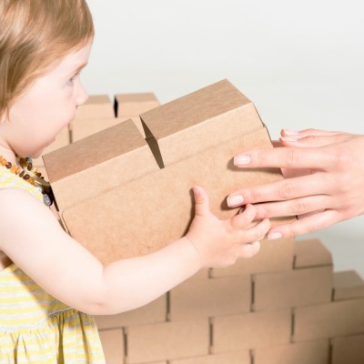Criança a segurar caixa de cartão castanha e mão adulta a ajudar
