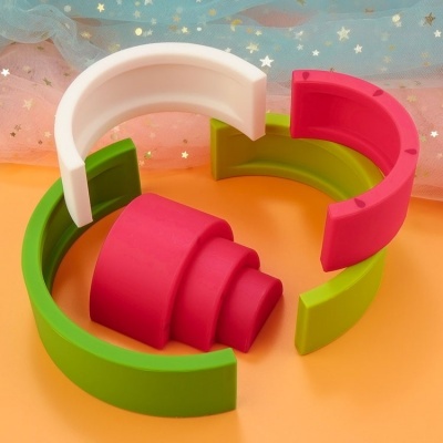 Peças de brinquedo empilháveis coloridas em semi-círculos sobre fundo laranja e tecido azul com estrelas