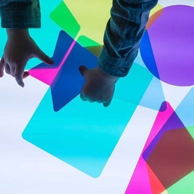 Mãos de criança segurando pedaços coloridos de plástico translúcido sobre superfície iluminada