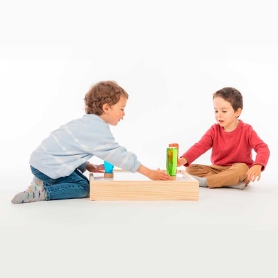 Duas crianças a jogar com tabuleiro de madeira e vaso com planta verde