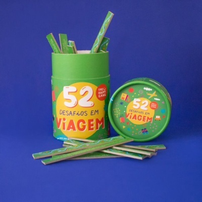 Conjunto de palitos verdes em recipiente cilíndrico verde com rótulo amarelo e laranja '52 Desafios em Viagem' sobre fundo azul