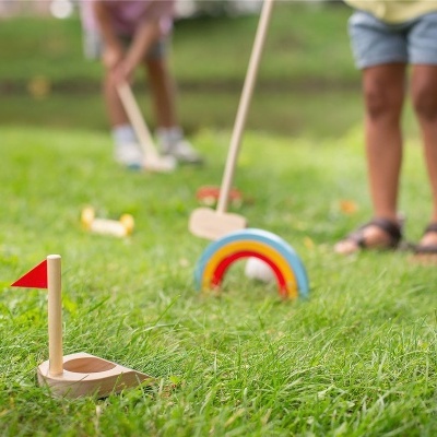 Jogo de mini-golfe infantil com tacos de madeira coloridos na relva.