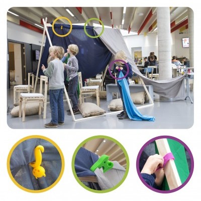 Crianças a brincar com estrutura de madeira e tecido azul e branco, ganchos coloridos e almofadas.