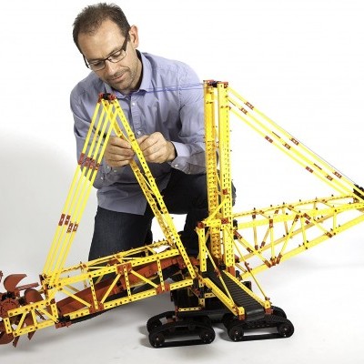 Homem montando modelo de grua amarela com esteiras pretas