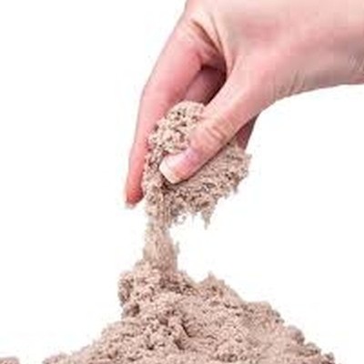 Mão segurando areia fina cinzenta sobre uma superfície com mais areia.