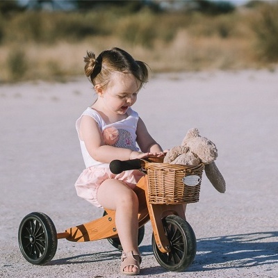 Menina em bicicleta de equilíbrio de madeira com cesto e peluche ao ar livre