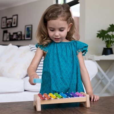 Menina com vestido azul turquesa a tocar xilofone colorido de madeira numa mesa