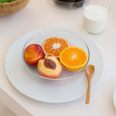 fruta artificial em prato de vidro em cima de prato branco com colher de madeira e copo de leite ao fundo