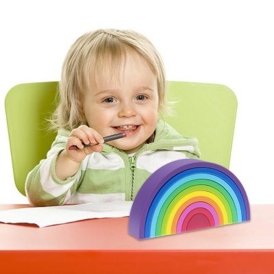 Criança sorridente com casaco verde e branco sentada numa mesa com brinquedo arco-íris colorido