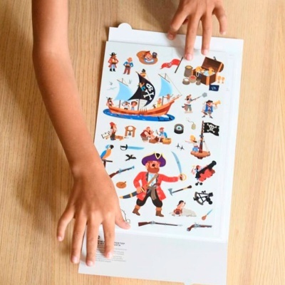 Ilustrações coloridas de piratas em folha branca sobre mesa de madeira clara com mãos de criança